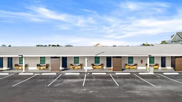 A motel with multiple rooms, each with a door and a window. There is a parking lot in front of the motel.