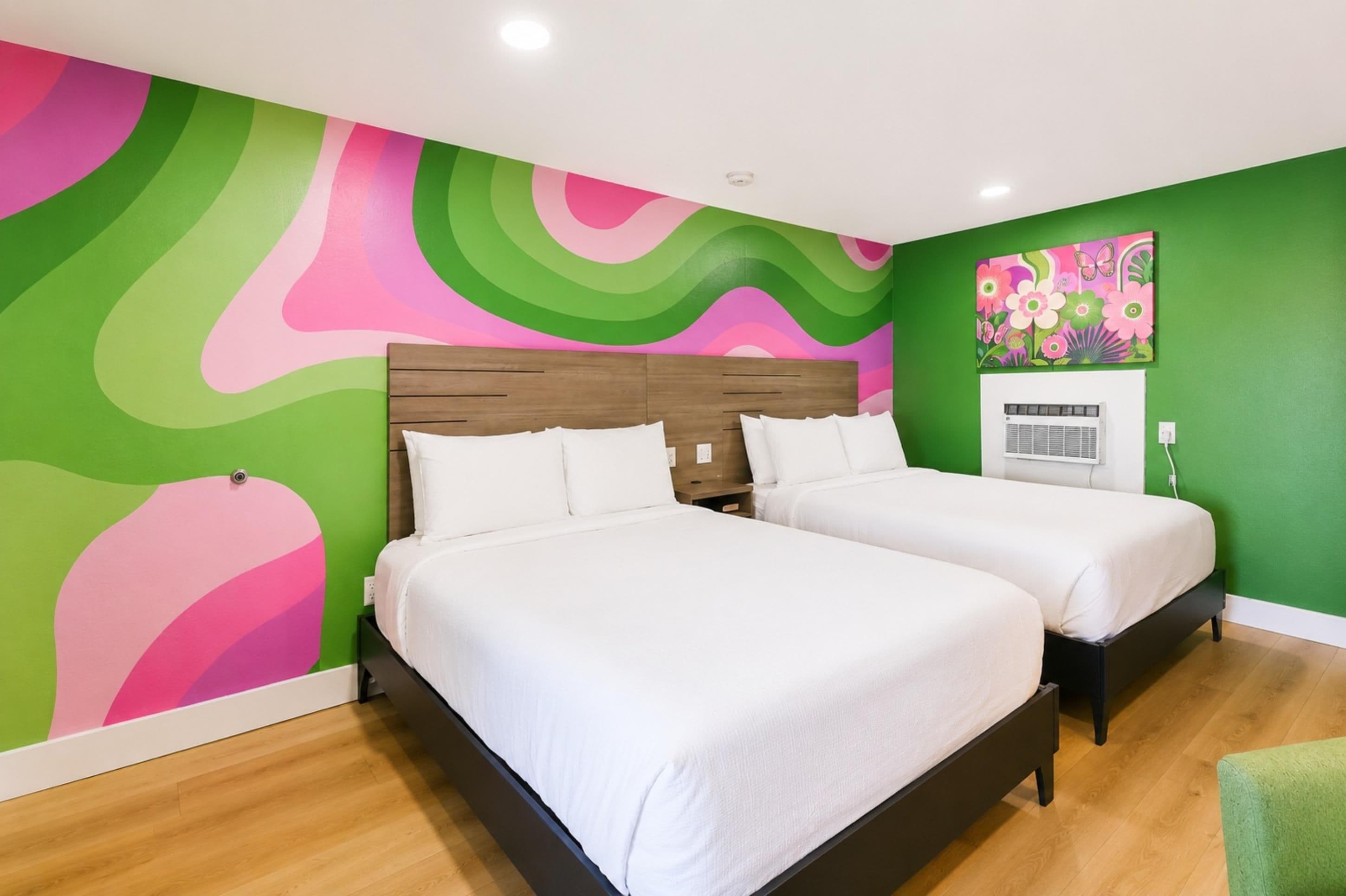 A room with two beds, a green wall, and a colorful abstract mural.