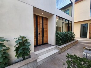 Un bâtiment moderne avec une porte en bois, un escalier menant à l’entrée et une grande fenêtre.