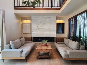 Un salon moderne avec une cheminée, deux canapés, une table basse et un balcon offrant une vue dégagée.