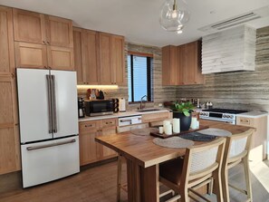 A modern kitchen with wooden cabinets, a white refrigerator, a microwave, a stove, and a dining area with a wooden table and chairs. - Private Rooftop Loft at Jackson Market (Culver City)