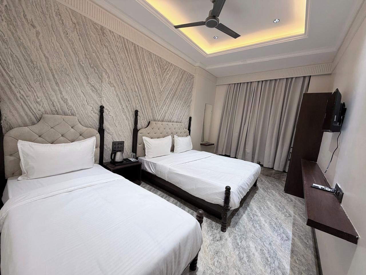 Habitación de hotel con dos camas, ventilador de techo, televisor de pantalla plana y pared con diseño de mármol.