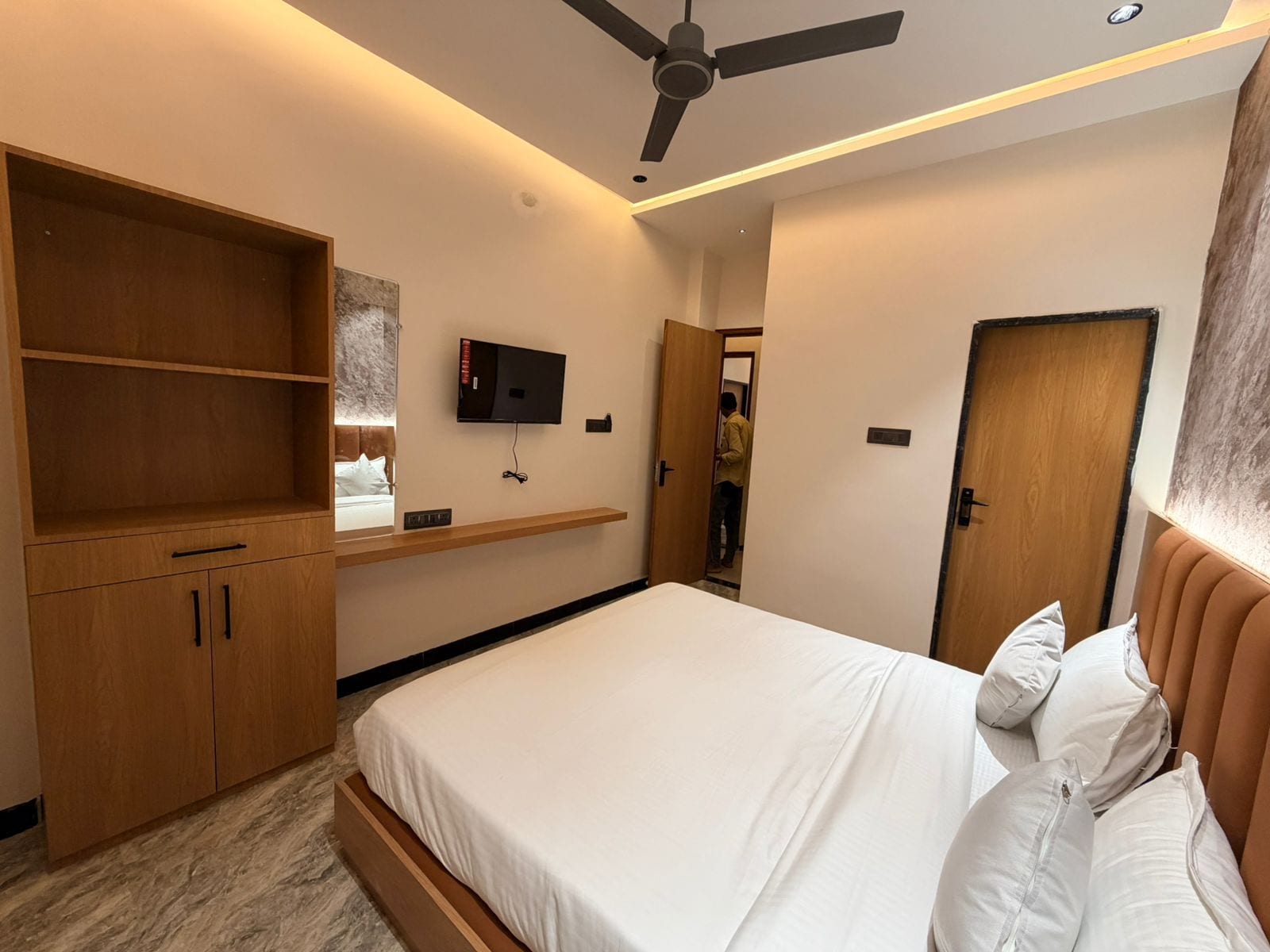 Un dormitorio moderno con una cama, armarios de madera, un televisor y un ventilador de techo.