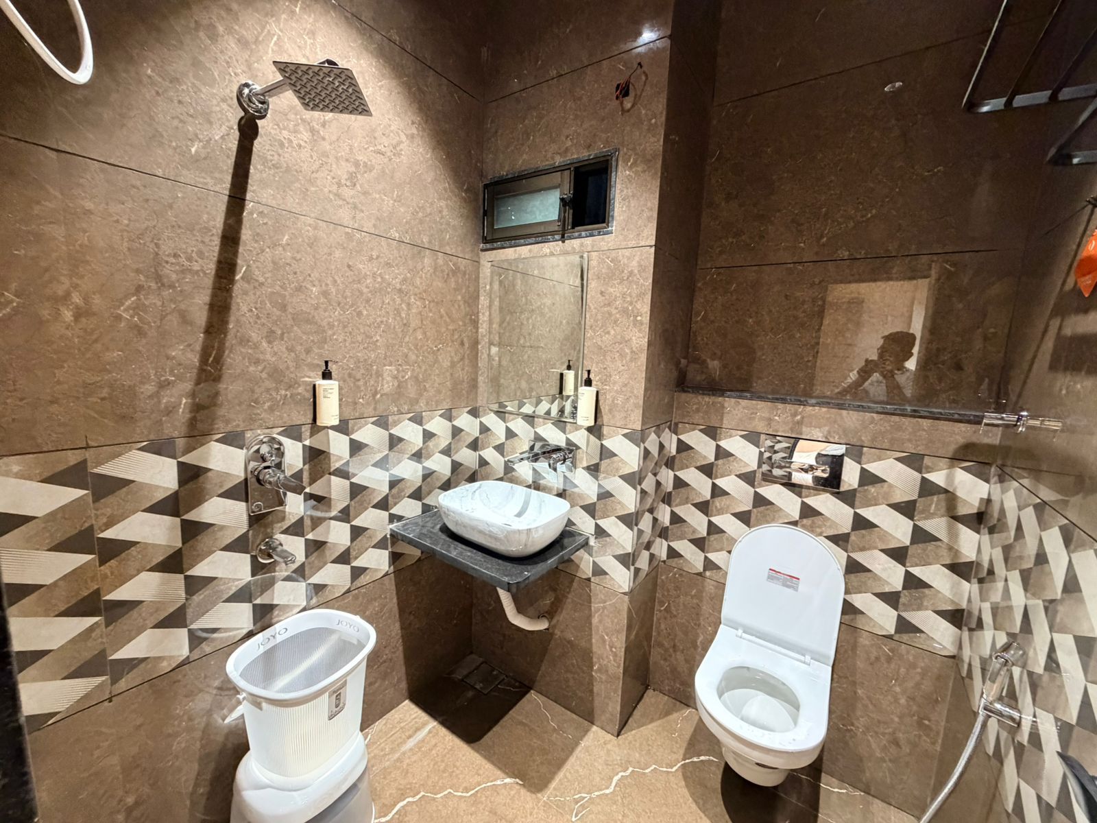 Un baño moderno con un diseño de baldosas geométricas, un lavamanos independiente, un inodoro y un cabezal de ducha manual.