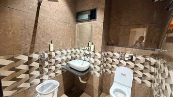 Un baño moderno con un diseño de baldosas geométricas, un lavamanos independiente, un inodoro y un cabezal de ducha manual.
