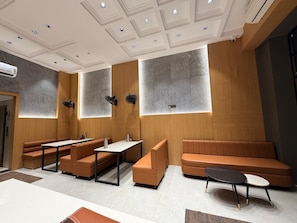 A modern interior with seating arrangements, a ceiling with recessed lighting, and a wall-mounted air conditioning unit. - Shree Mangalam Stays & Kitchen (Ujjain)