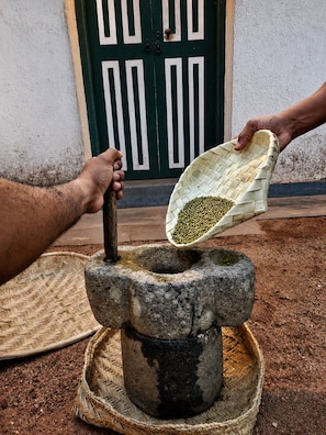 A person using a stone mortar and pestle to grind green seeds. - Piyasewana Spice Garden Villa (Banduragoda)