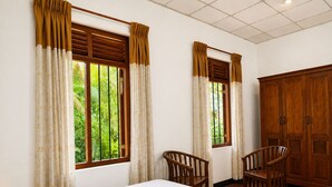A hotel room with two single beds, a wooden wardrobe, two wooden chairs, and windows with curtains. - Piyasewana Spice Garden Villa (Banduragoda)