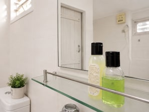 A bathroom with a glass shelf holding two bottles of shampoo and conditioner. - Piyasewana Spice Garden Villa (Banduragoda)