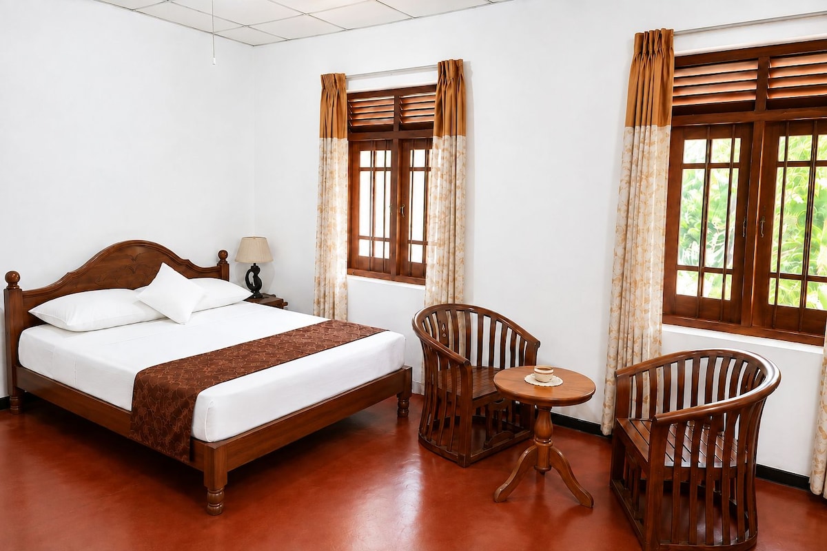 A hotel room with a wooden bed, two chairs, a small table, and windows with curtains.