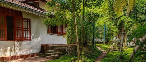 Una casa tradizionale con tetto in tegole, vialetto in pietra e vegetazione lussureggiante.