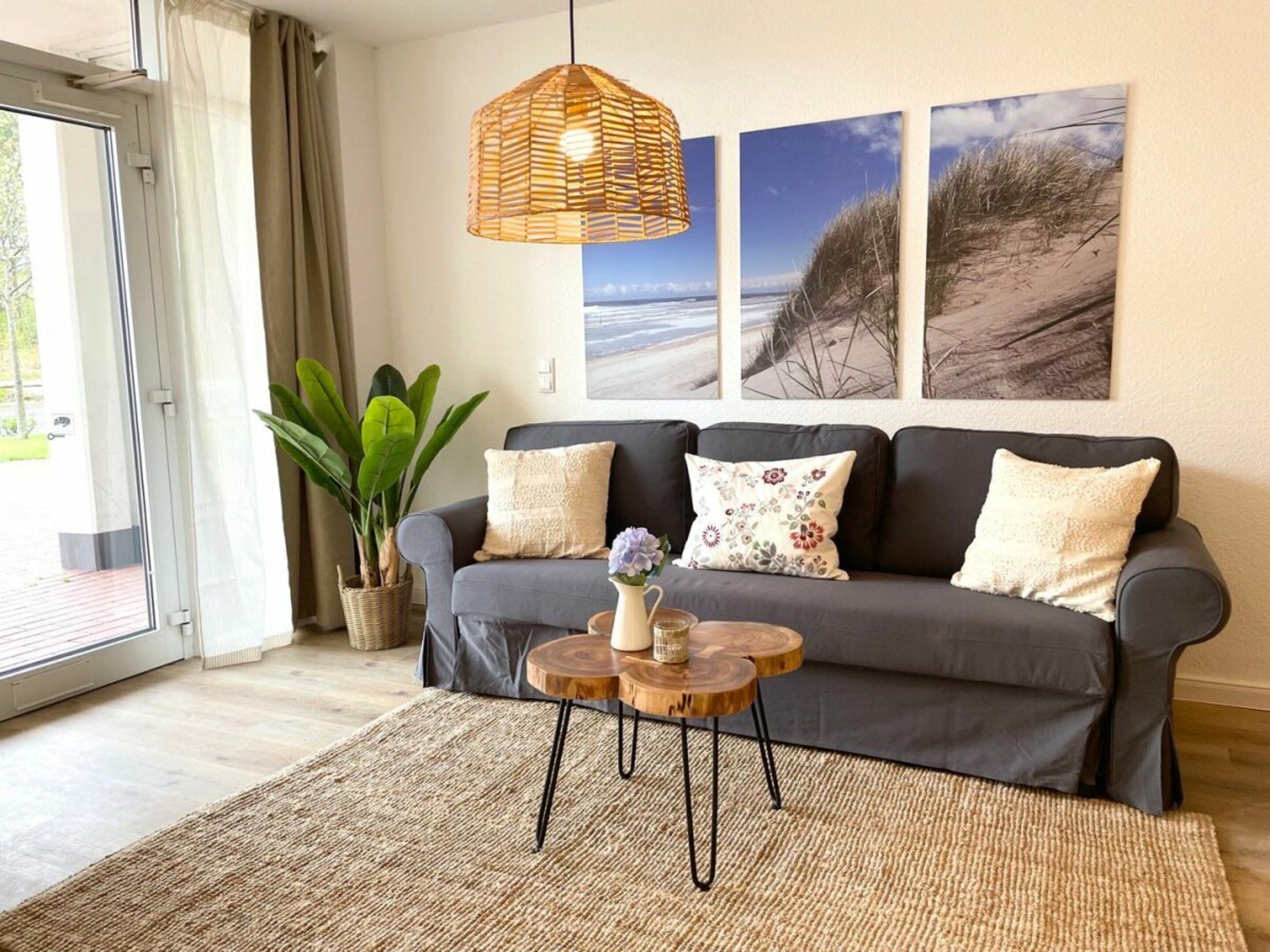 A living room with a grey sofa, a woven pendant light, a round wooden coffee table, and a large potted plant.