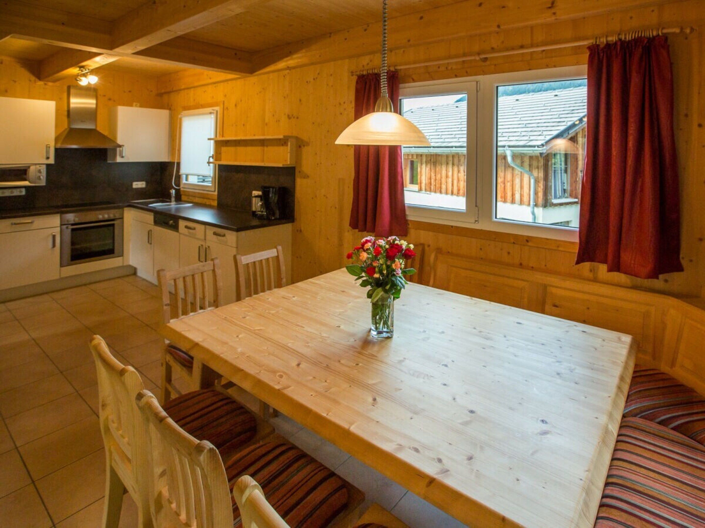 A wooden interior with a kitchen, dining table, chairs, and a vase of flowers.