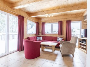 A wooden interior with a red sofa, a small table, and a chair. There are windows with curtains, a television, and a bookshelf. - Cabin in Annaberg With Swimming Pool (Annaberg-Lungoetz)