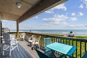 Um deck de madeira com móveis para área externa com vista para a praia.