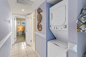 Uma lavanderia com máquina de lavar e secadora, um corredor que dá para um quarto e uma peça decorativa de um cavalo-marinho na parede.