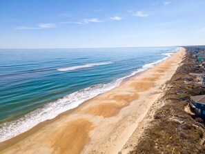 Ein Küstenstrand mit blauem Himmel, sandigem Ufer und einer Reihe von Gebäuden, von denen eine Treppe zum Strand führt.