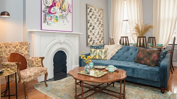 Een woonkamer met een blauwe bank, een gestreept fauteuil en een open haard.