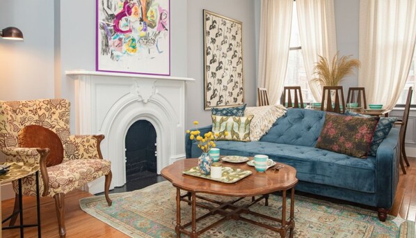 A living room with a blue sofa, patterned armchair, and a fireplace. - Classic NYC 3BR/1BA City Escape! Stay Near Central Park! (New York)