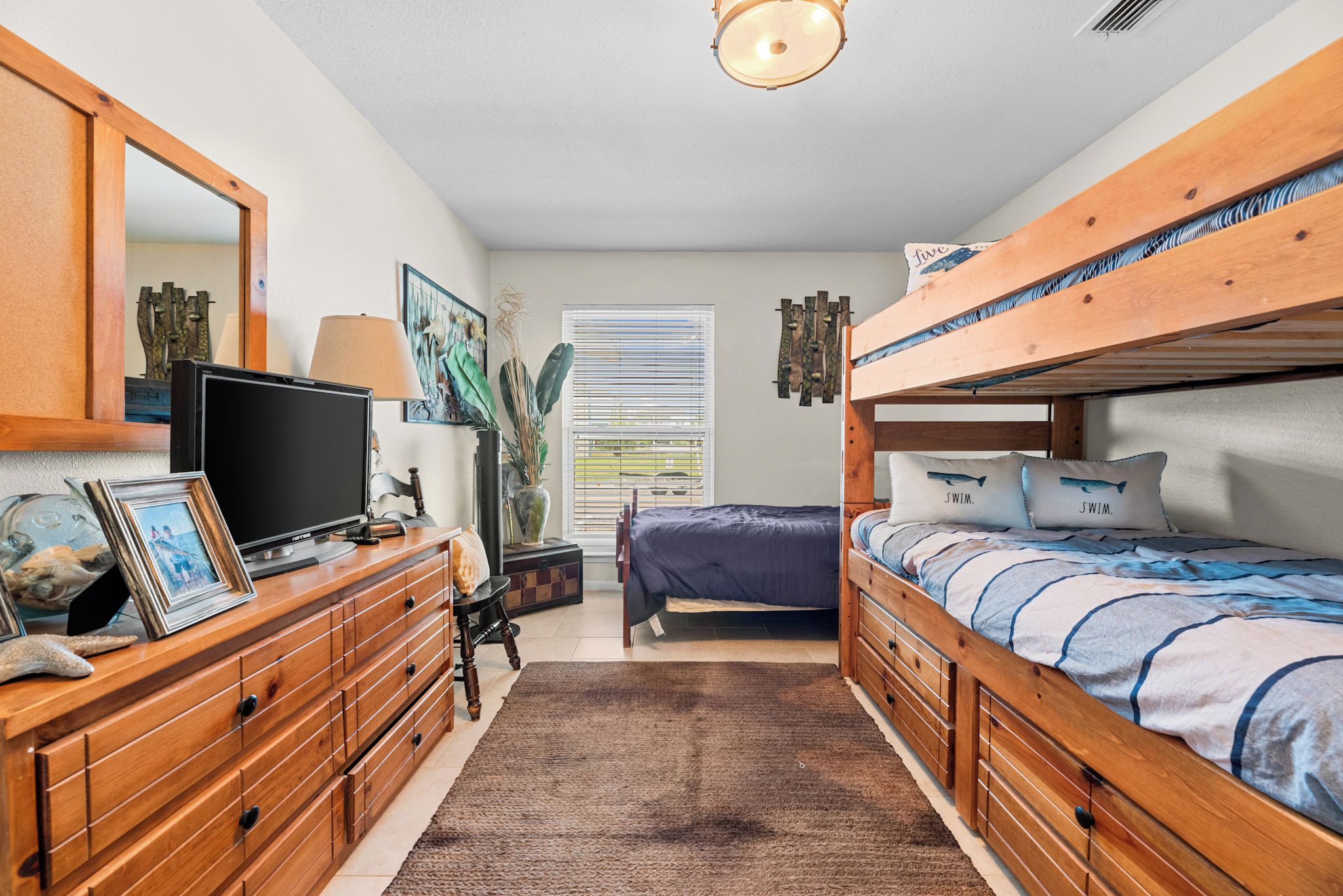 A bedroom with a bunk bed, a desk with a computer, a dresser, and a window with blinds.