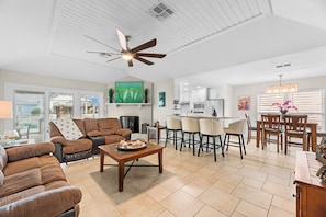 A spacious living room with a fireplace, a dining area with a kitchen in the background, and a ceiling fan. - Hook, Wine and Sinker ~3 Bed / 2 Bath Home with a Pool! (Rockport)
