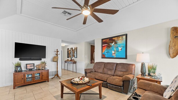 Ein Wohnzimmer mit braunem Sofa, Couchtisch, Fernseher und Deckenventilator.
