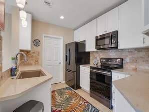 A kitchen with white cabinets, stainless steel appliances, a microwave, and a patterned rug. - Spacious 3-bedroom condo with AC in peaceful Vero Beach (Vero Beach)