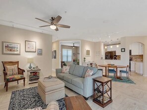 A living room with a sofa, ottoman, and coffee table, a dining area with a table and chairs, and a kitchen in the background. - Spacious 3-bedroom condo with AC in peaceful Vero Beach (Vero Beach)