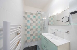 Ein modernes Badezimmer mit Dusche, einer Duschkabine aus Glas, einem weißen Waschbecken und einem Spiegel darüber.
