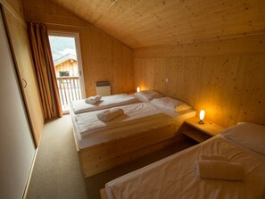 Ein Zimmer in einer Holzhütte mit zwei Betten, einem Fenster und Blick auf eine Holzkonstruktion draußen.