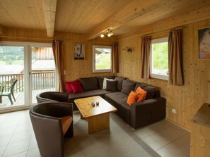 A wooden interior with a sofa, a coffee table, and a chair. There are windows with curtains, a picture on the wall, and a view of the outdoors. - Cabin in Annaberg With Swimming Pool (Annaberg-Lungoetz)