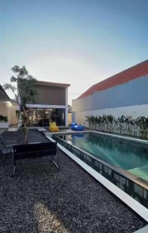 Una piscina con un bordeado de baldosas, rodeada de edificios con techo rojo y pared azul.