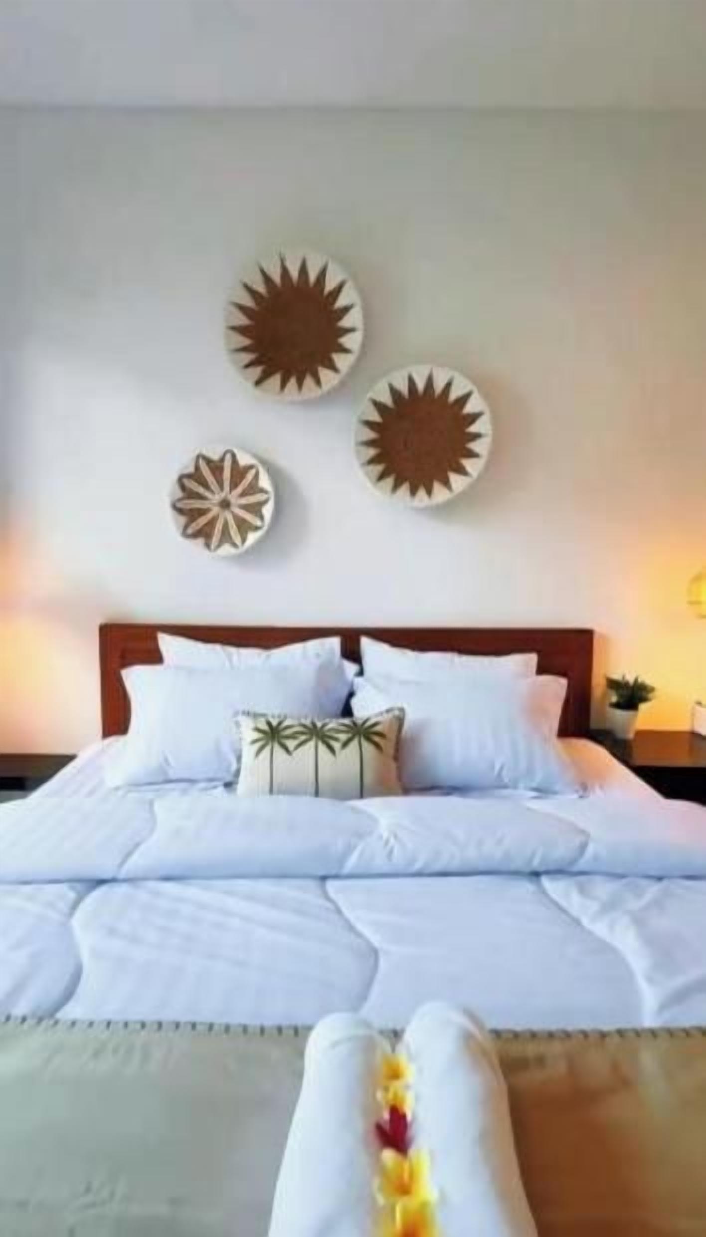 Een netjes opgemaakt bed met witte beddengoed en decoratieve kussens, een houten hoofdbord en wanddecoratie erboven.