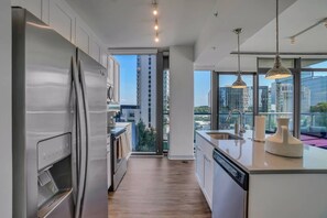 Una cocina moderna con un refrigerador de acero inoxidable, lavavajillas y un amplio ventanal con vista a la ciudad.