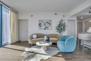 A modern living room with a sofa, a blue armchair, a coffee table, a painting, and a potted plant. - Top Tier Panoramic Skyline Views High-Rise! (Atlanta)