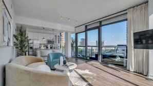 Un soggiorno moderno con una grande finestra, una TV a schermo piatto e un'area pranzo con cucina sullo sfondo.