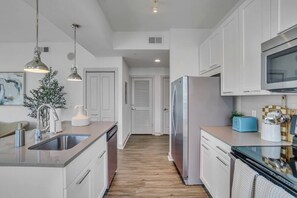 Une cuisine moderne dotée d’appareils électroménagers en acier inoxydable, de meubles blancs et d’un plancher en bois.