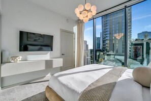 Habitación de hotel moderna con una cama grande, televisor montado y balcón con vista a la ciudad.