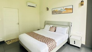 A hotel room with a bed, bedside table, wall-mounted air conditioning unit, and a painting. - WAYANAD DE MOUNT RESORT BY RAK ROOMS (KL)