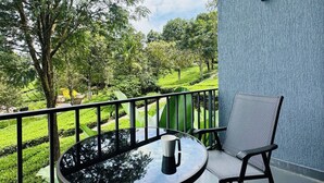 A balcony with a table and chair, a view of a green landscape, and a textured wall. - WAYANAD DE MOUNT RESORT BY RAK ROOMS (KL)