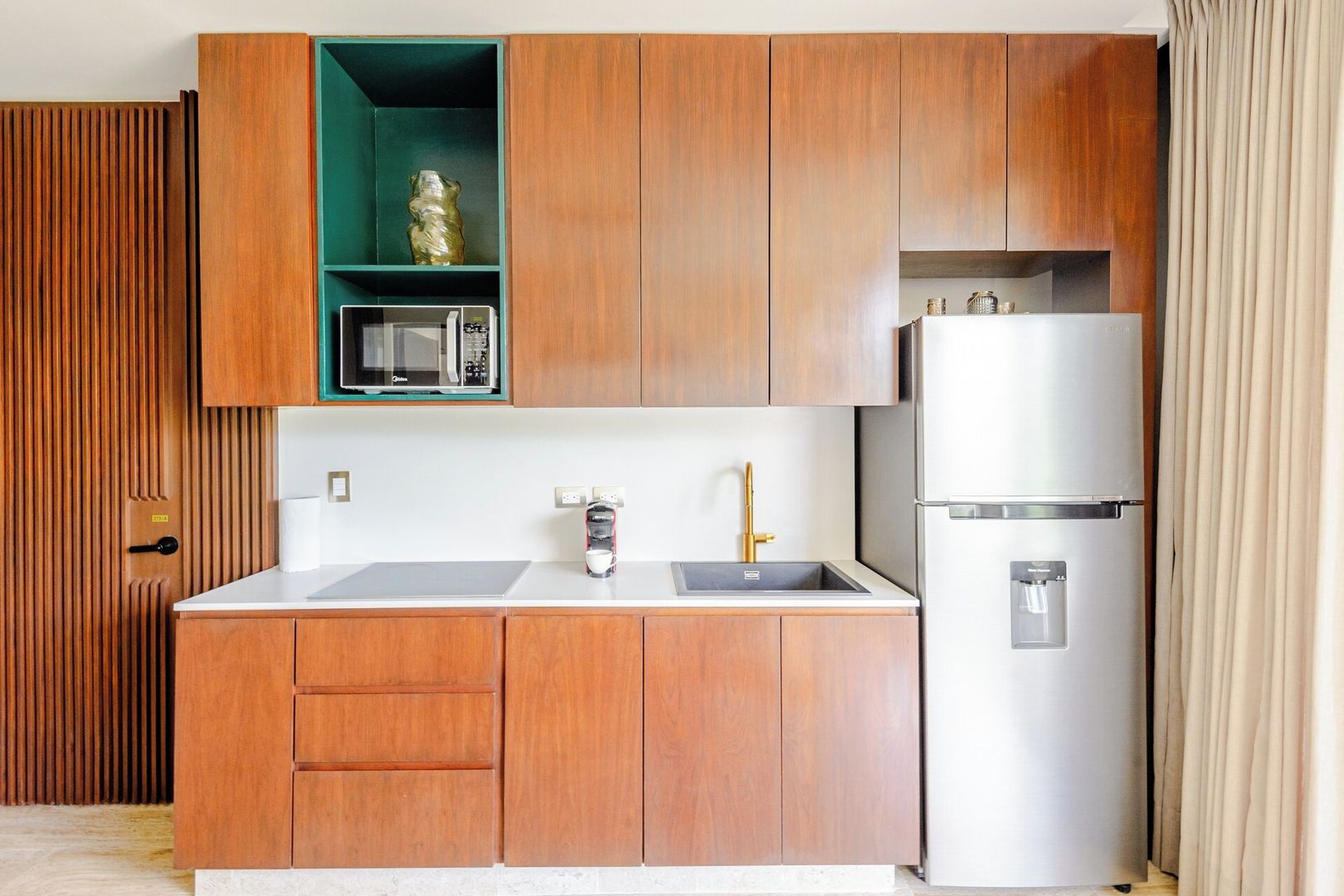 Une cuisine compacte avec des meubles en bois, un four à micro-ondes, un évier avec un robinet et un réfrigérateur.