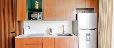 A compact kitchen with wooden cabinets, a microwave, a sink with a faucet, and a refrigerator.
