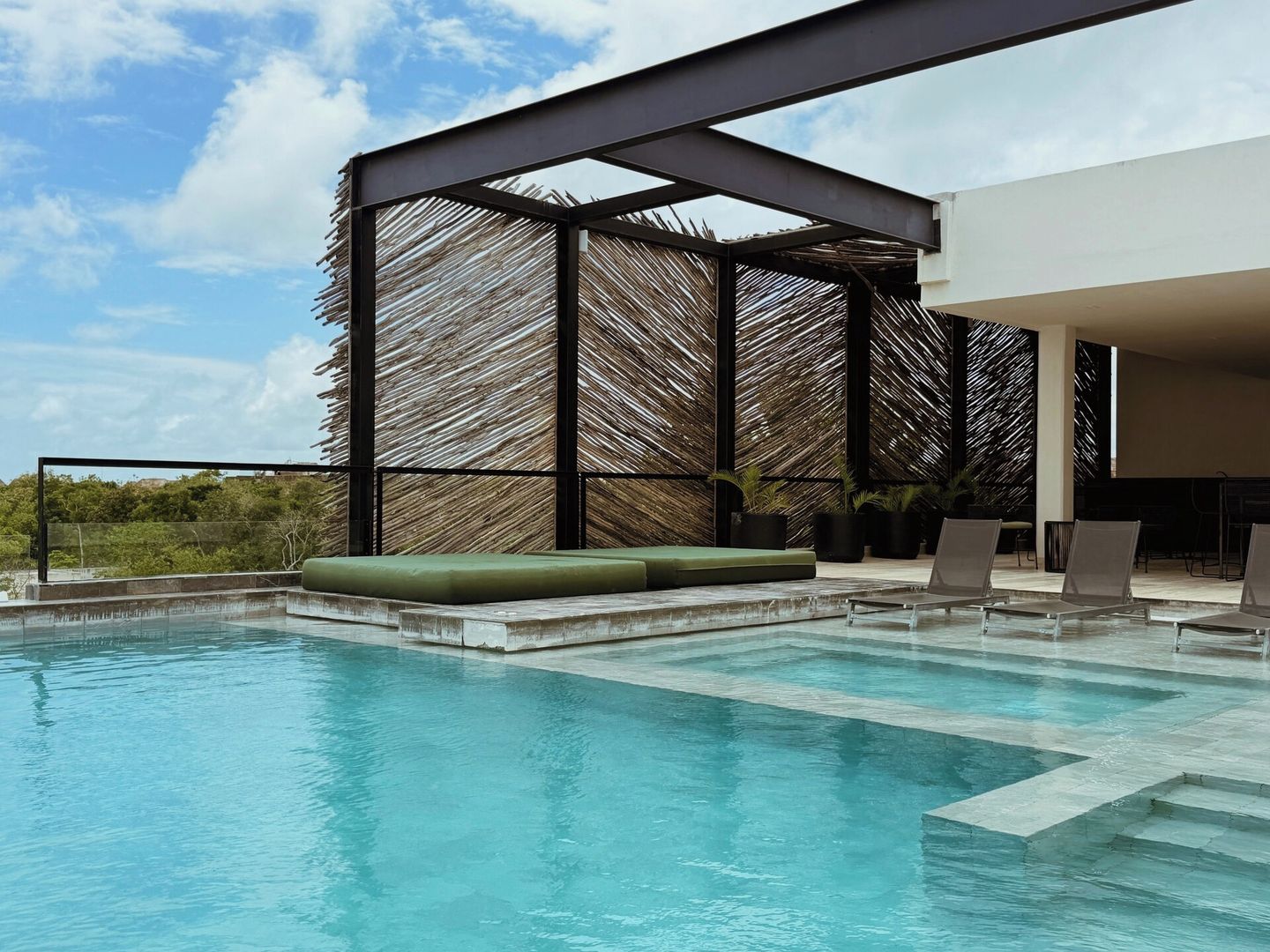 A rooftop pool area with a clear view of the sky, a thatched structure, and lounge seating.