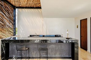 A modern kitchen with a marble countertop, two bar stools, and a built-in sink. - 2 bedrooms Penthouse w/ Private jungle terrace (Tulum)