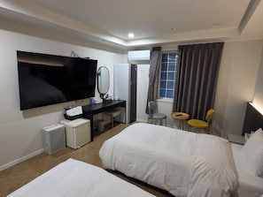 Hotellihuone, jossa on sänky, työpöytä, jossa on litteänäyttöinen televisio, peili, ikkuna verhoilla sekä pieni pöytä tuoleineen.