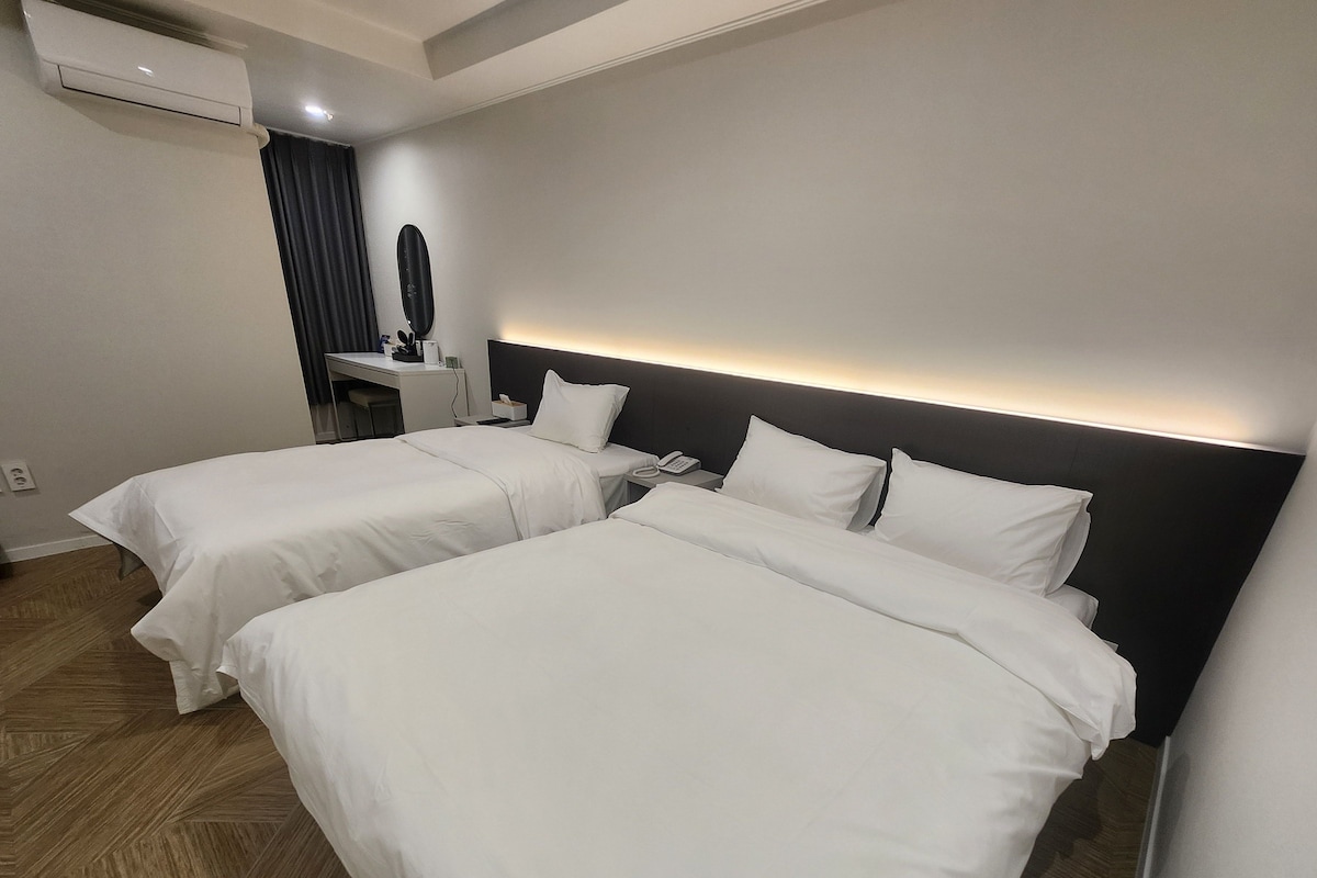 Hotellihuone, jossa on kaksi sänkyä, työpöytä ja peili.