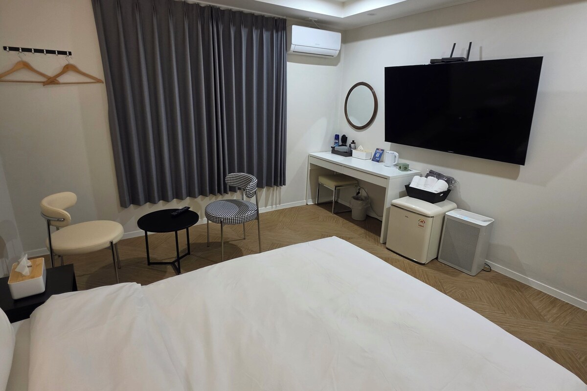 Hotellihuone, jossa on sänky, työpöytä tuolilla, televisio ja ilmastointilaite.