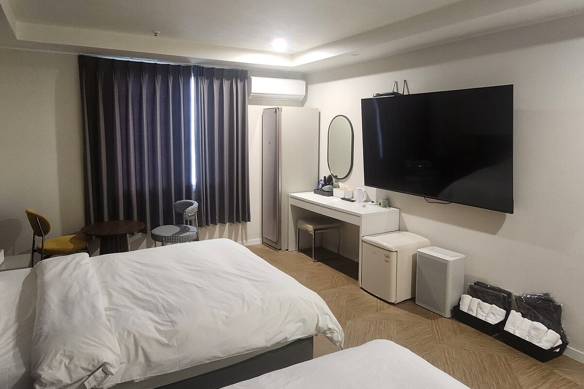 Hotellihuone, jossa on kaksi sänkyä, kirjoituspöytä peilillä, televisio ja tuoli.