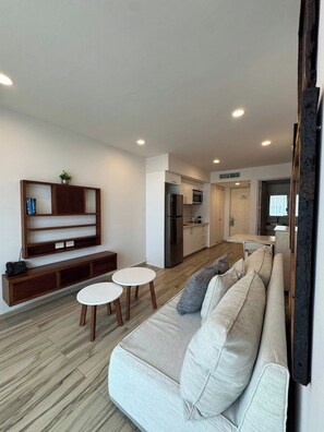 A modern living room with a sofa, two small tables, a wooden console, and a kitchen in the background. - King 1BR · 1.5 Baths · Rooftop Pool · 5th Ave (Playa del Carmen)