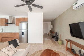 A modern living room with a sofa, a television, and a ceiling fan. - Aldea Zama · 2BR with pool · Guest favorite (Tulum)